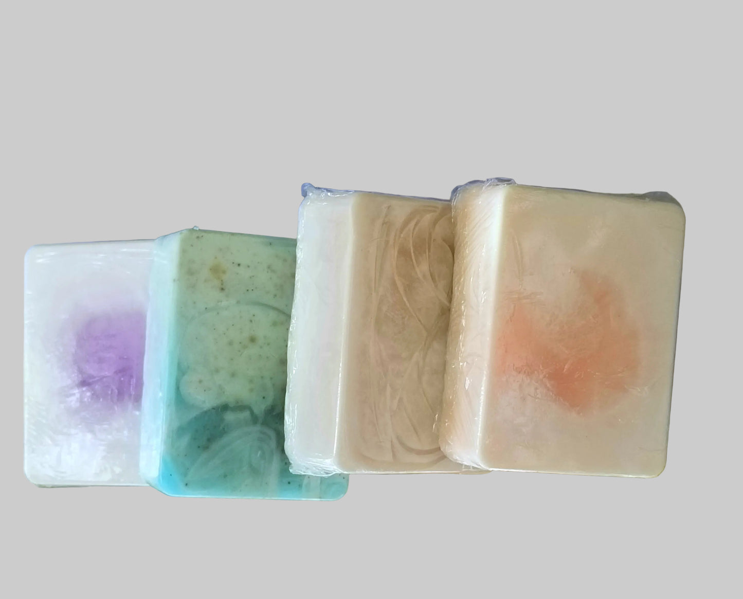 Three bars of handmade soap, each with a different color and scent, displayed on a surface with a background that includes a cloudy sky and distant hills.